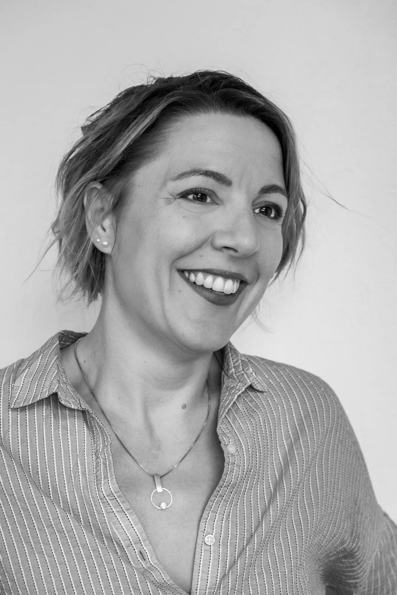 Portrait souriant d'une femme en chemise rayée, noir et blanc.