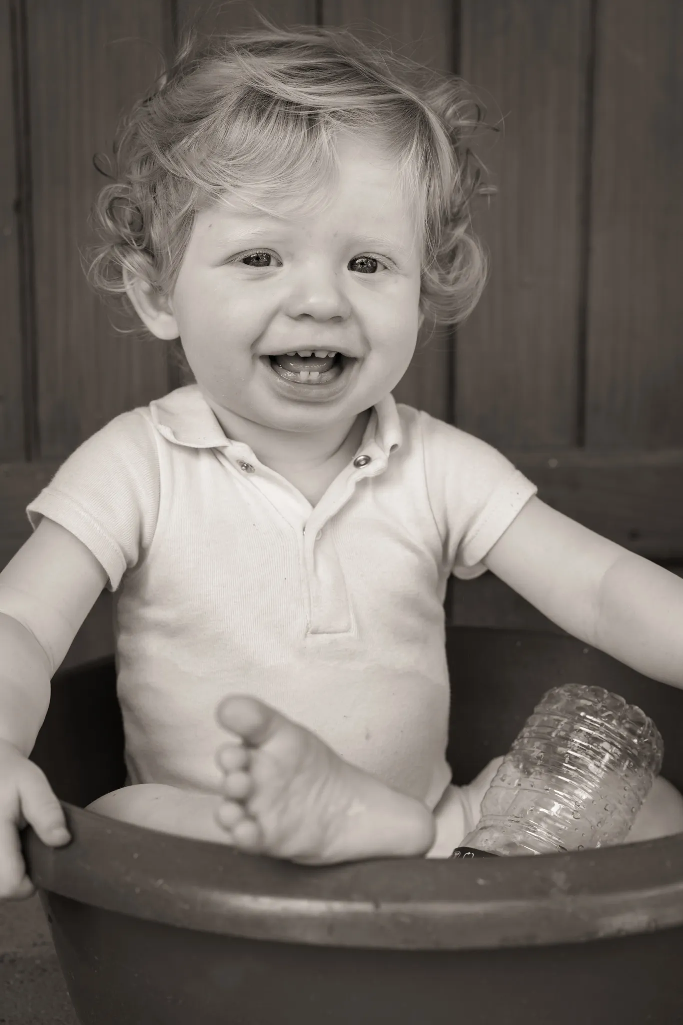 Bébé souriant avec quelques dents, assis dans une bassine d'eau.
