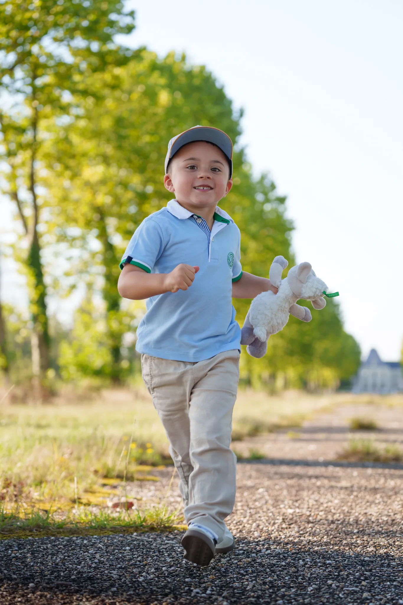 Jeune garçon rieur qui court sur un chemin ensoleillé, avec son doudou à la main.