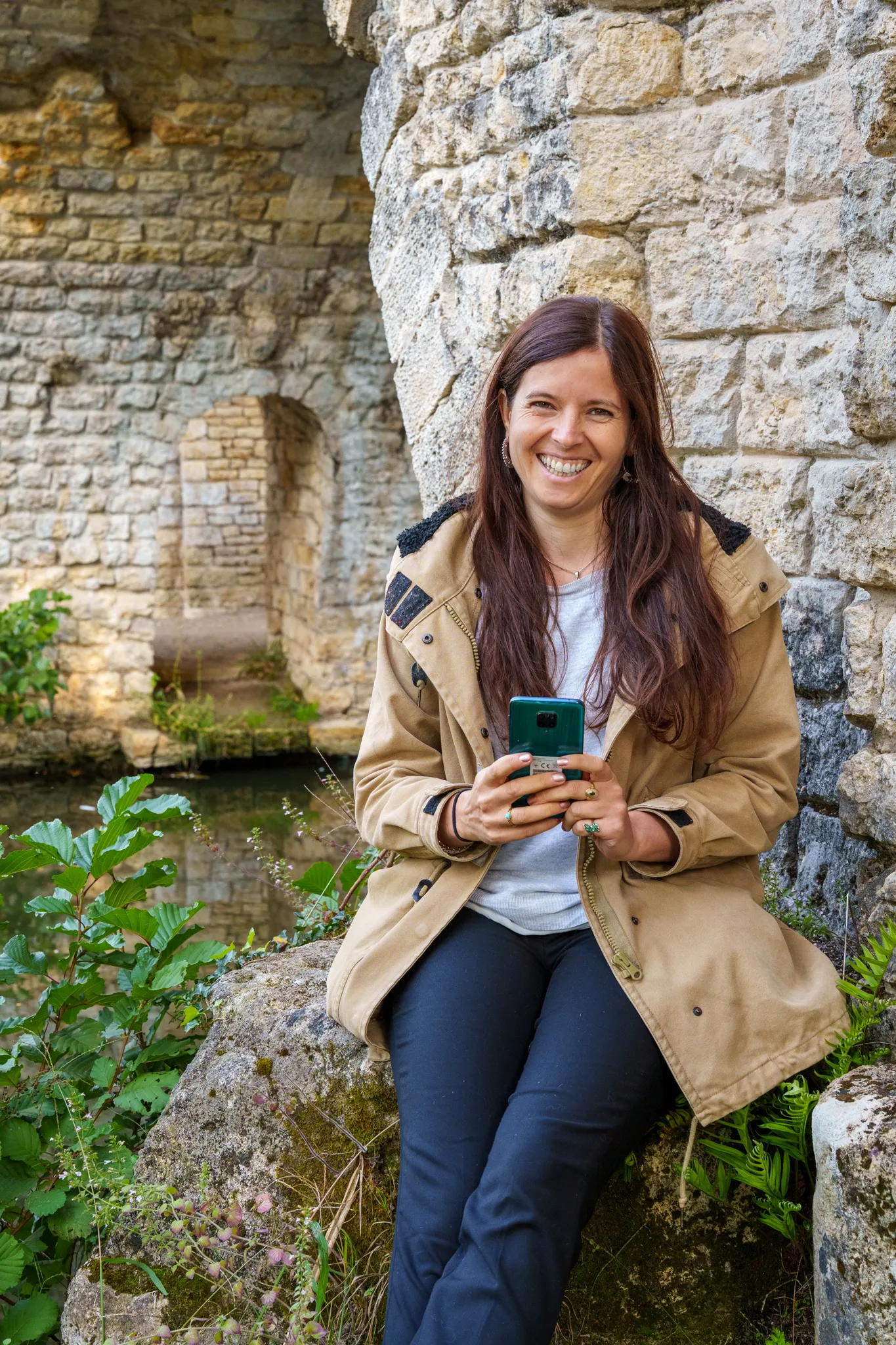 Coach pro souriante et téléphonant, à côté d'un mur pont de pierre.