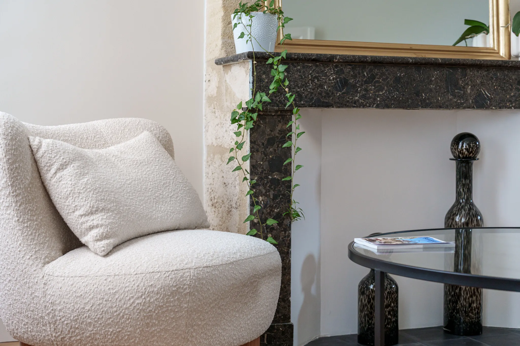 Fauteuil en bouclette écru devant cheminée pierre et marbre noir
