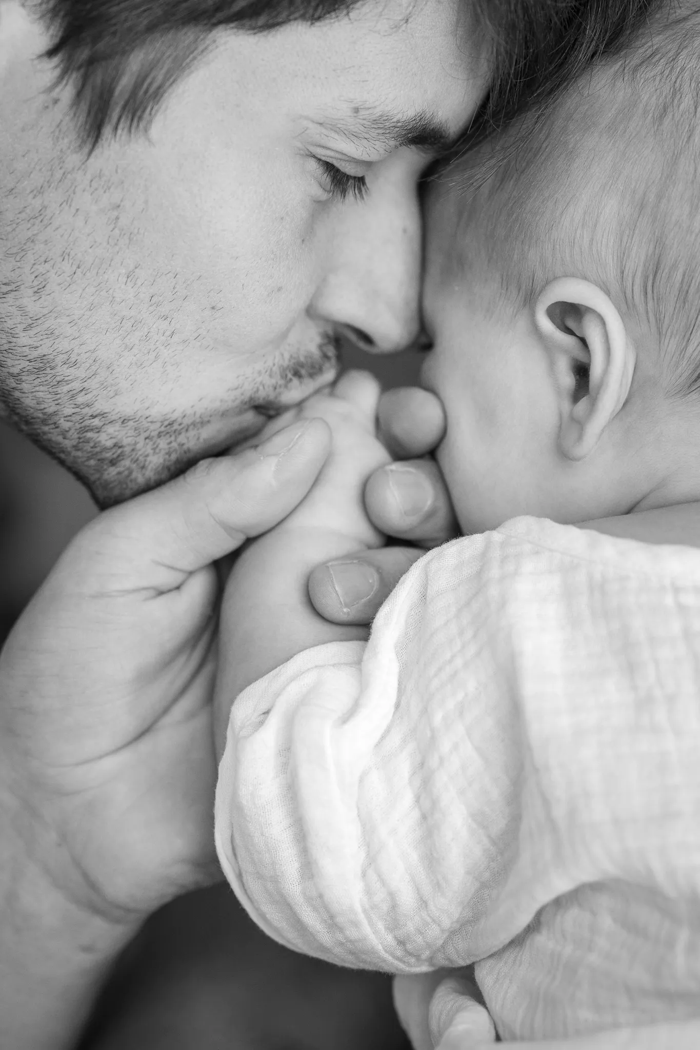 Profil d'un papa, embrassant son bébé vu de dos, noir et blanc.