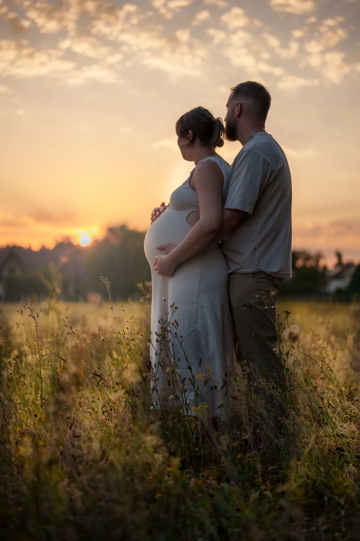 Futurs parents enlacés dans un champ au coucher du soleil.