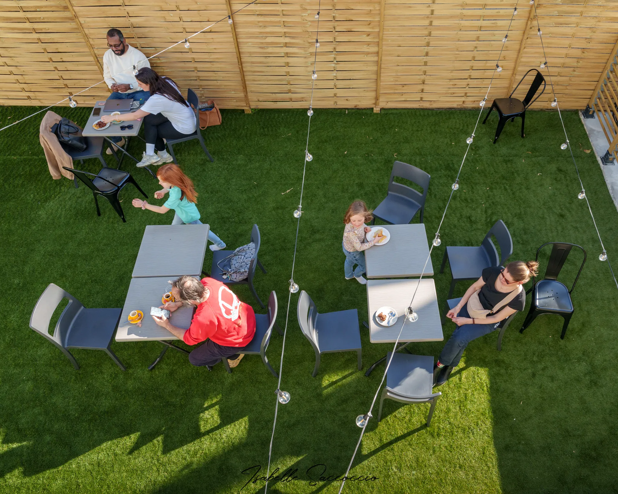 Vue plongeante sur cour d'une terrasse verdoyante, avec des clients et enfants.
