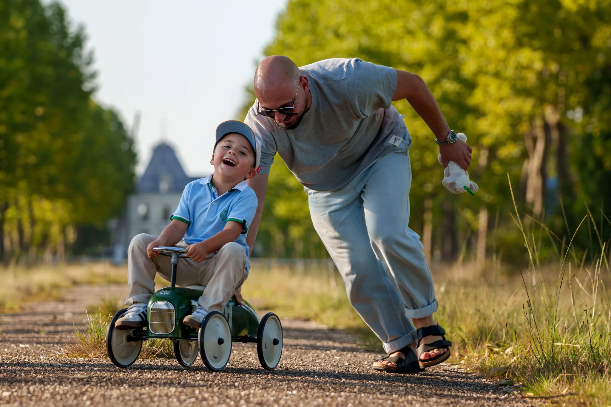 Père poussant son enfant rieur assis sur une voiture jouet.
