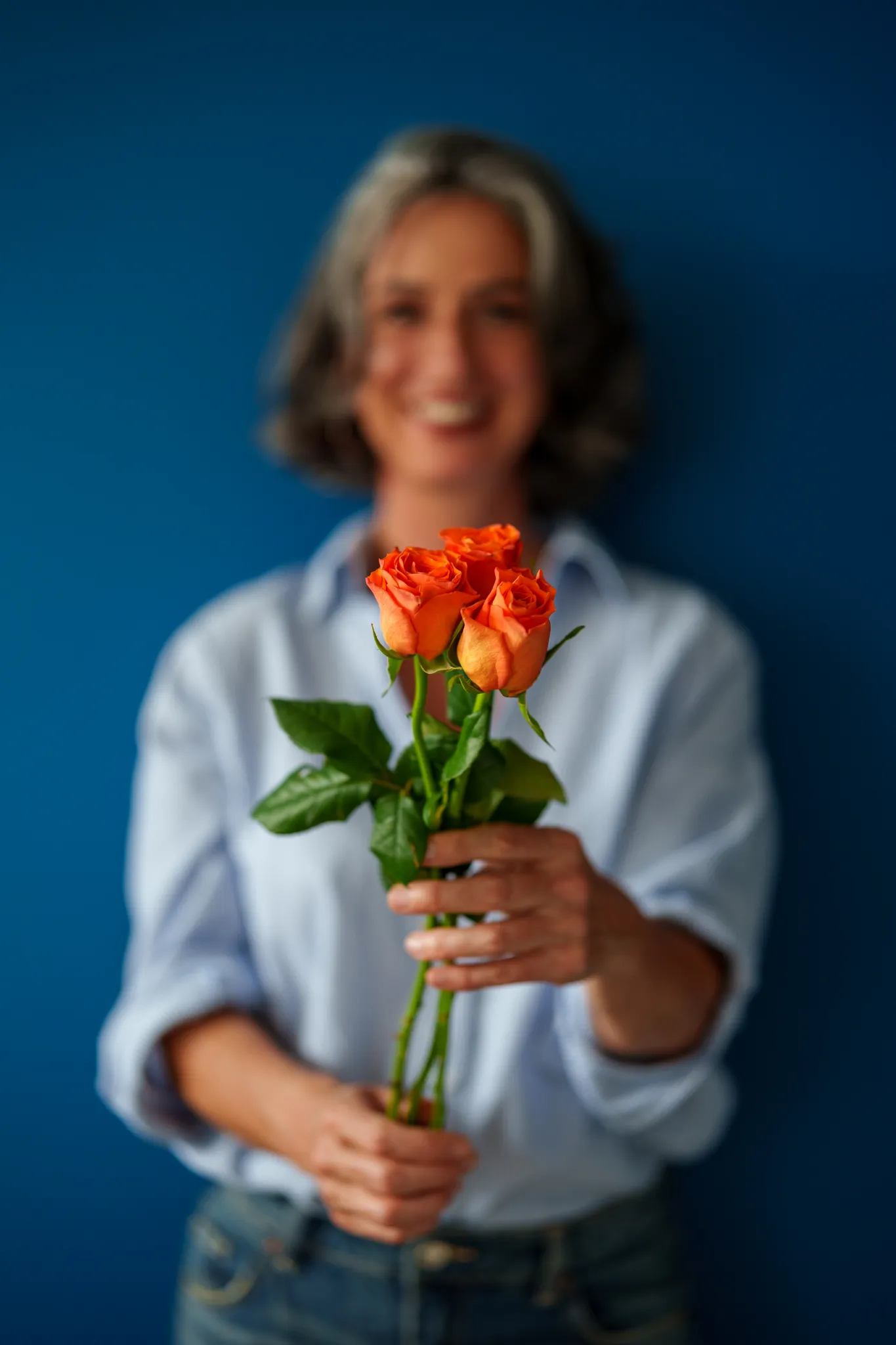 Portrait flou tenant des roses oranges sur fond bleu.