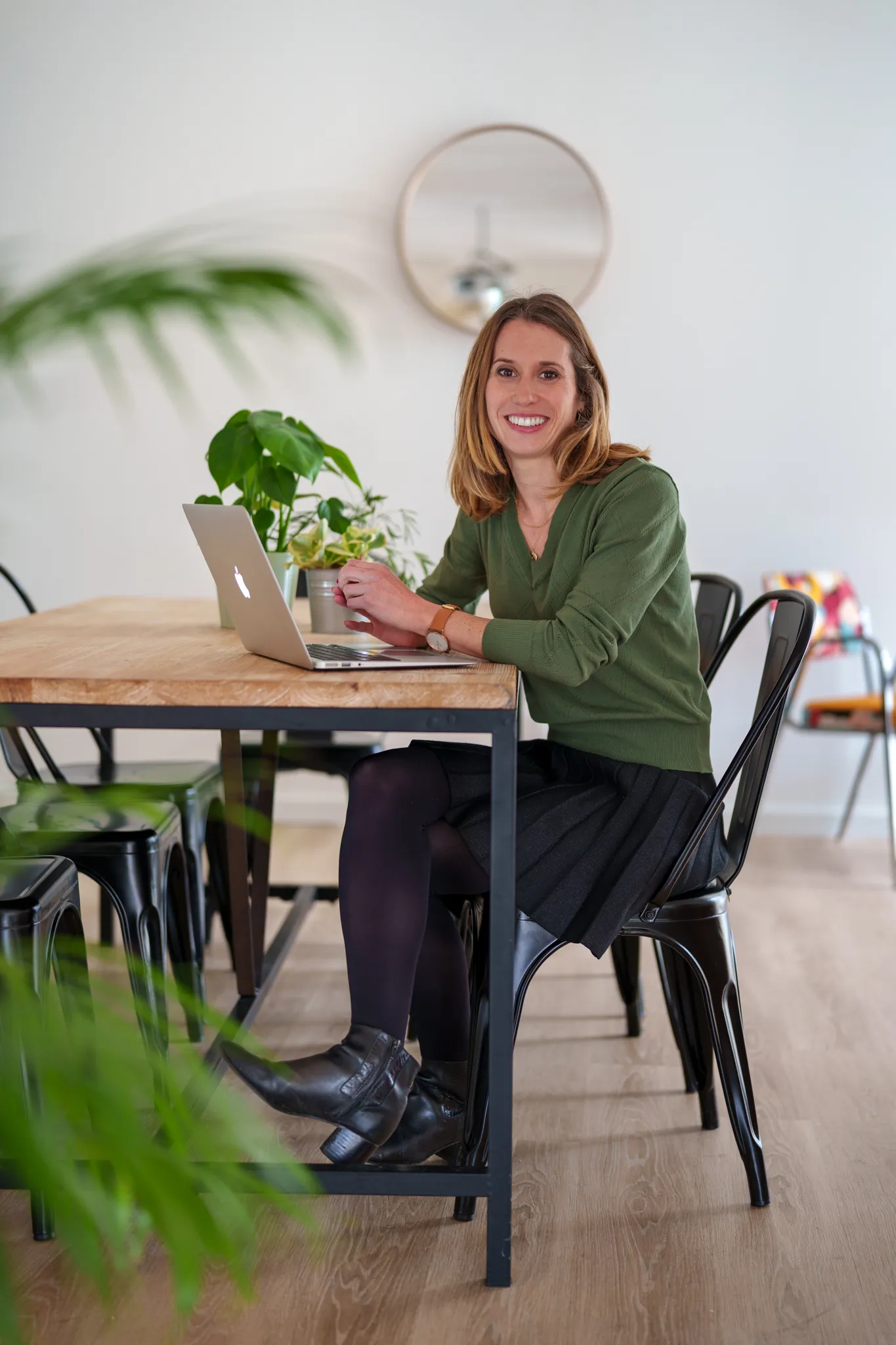 Entrepreneuse travaillant sur ordinateur, assise à table dans un intérieur lumineux.