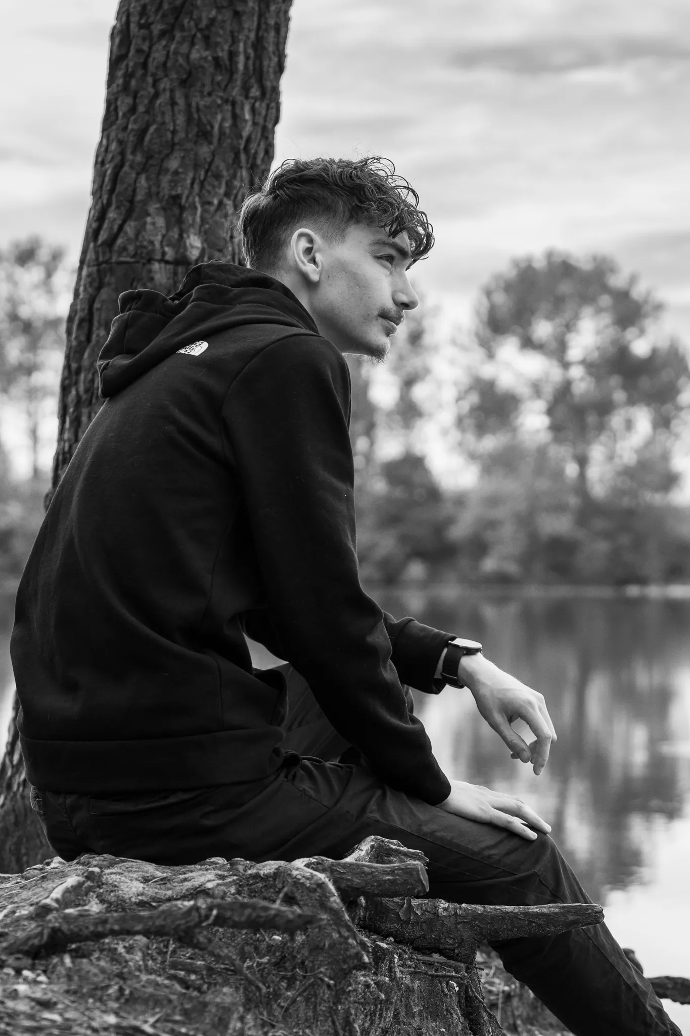 Jeune homme assis au bord de l'eau, vue de dos, en forêt.