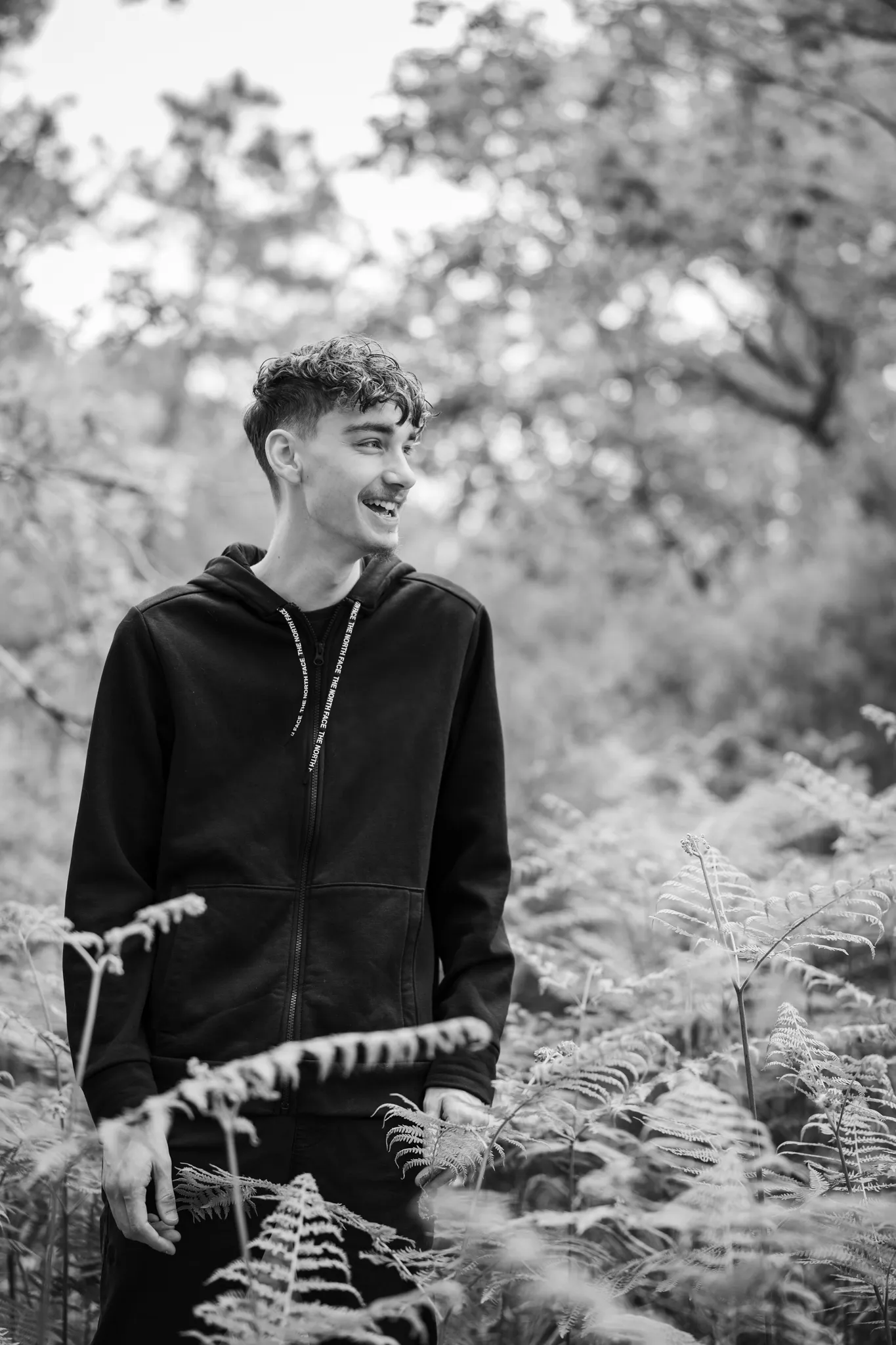 Jeune homme rieur, au milieu de fougères dans les bois, noir et blanc.