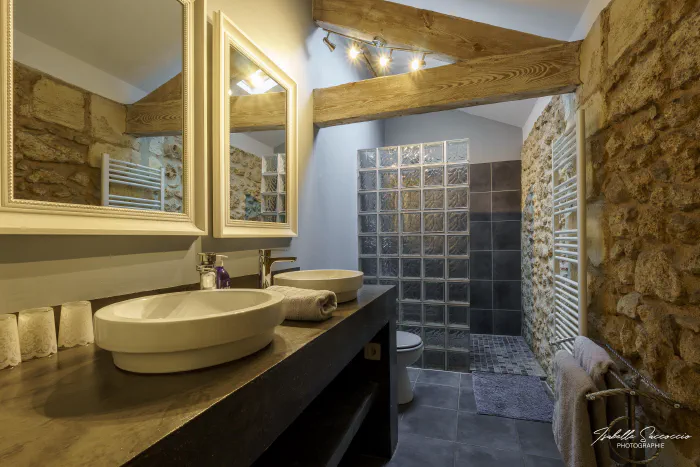 photo immobiliere pour gite d'une jolie salle de bain sous les toits avec murs en pierres apparentes et poutres - photo par Isabelle SACCOCCIO